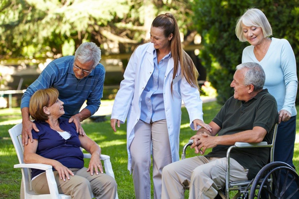 Many seniors relaxing in a park of a nursing home with geriatric nurse