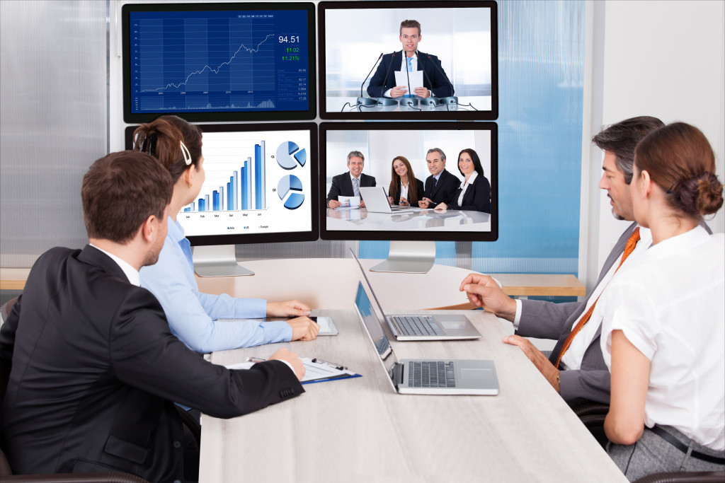 group of employees sitting at a desk while looking at monitors with business people